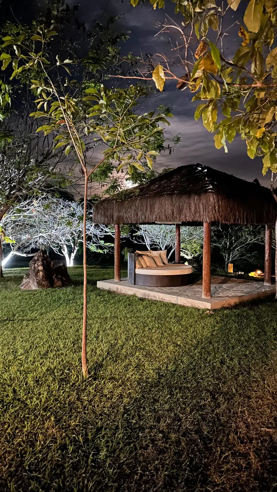 Quiosque de palha com daybed no gramado do hotel à noite